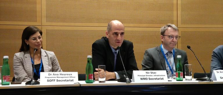 Three individuals sit at a panel table with nameplates and microphones. From left to right: Dr. Ana Heureux, Niri Stav, Dr. Nathan D.