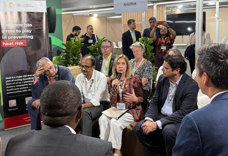 A group of people sits in a circle having a discussion at an event; a sign reading 