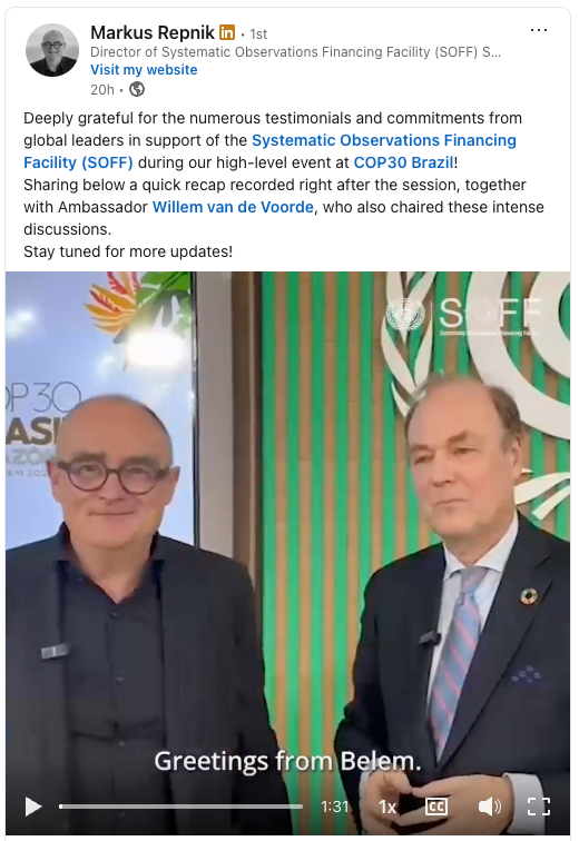 Two men in suits stand side by side, smiling at the camera with a banner behind them reading 