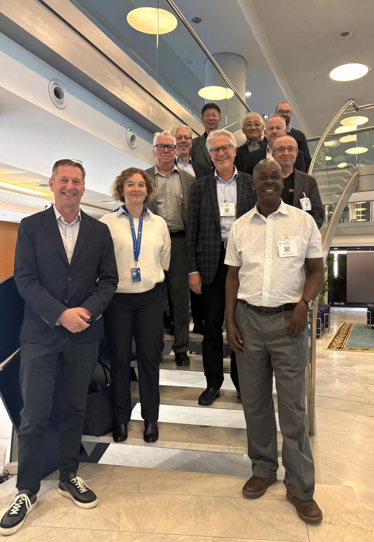 A group of eleven adults, dressed in business casual attire, stand and smile on an indoor staircase in a modern building.