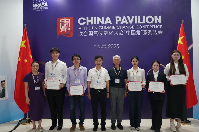 A group of eight people stands in front of a "China Pavilion" banner at the UN Climate Change Conference; five hold certificates, two Chinese flags are displayed on each side.