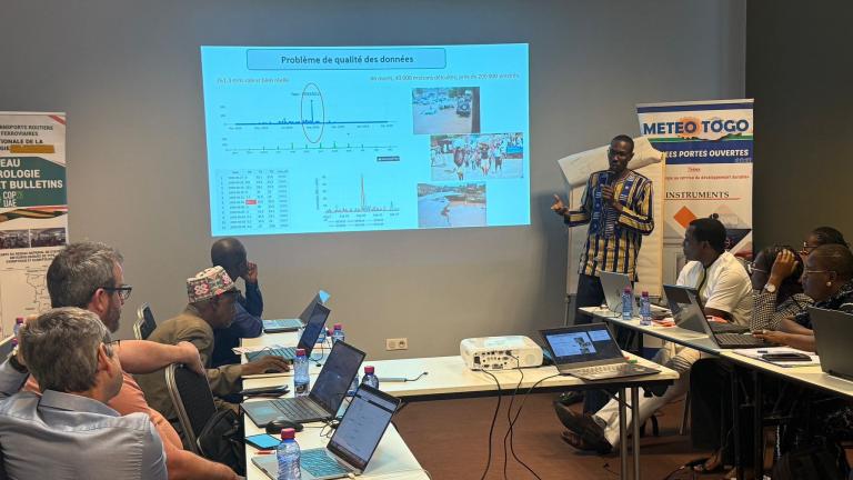A presenter stands and points to a projected data quality problem slide in French, while several seated participants with laptops listen in a conference room.