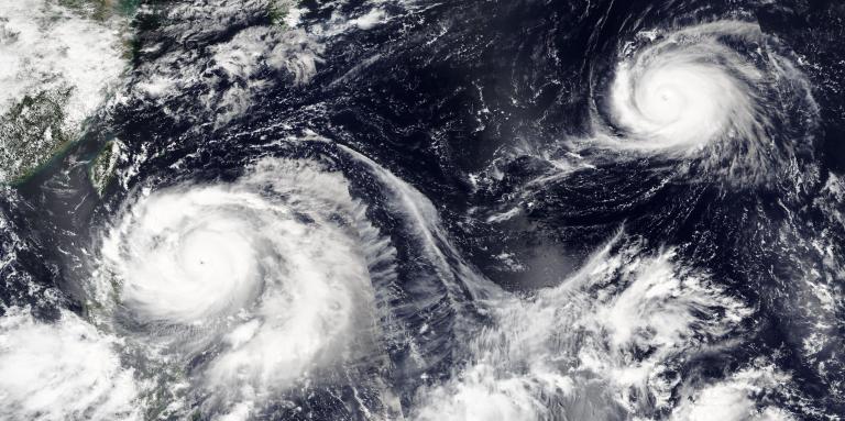 Satellite image showing two large cyclones swirling over the ocean, with visible cloud bands and eye formations.