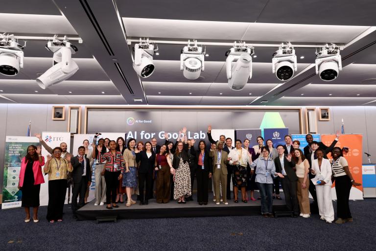 A large group of people stand together on a stage, posing for a photo at an event with 