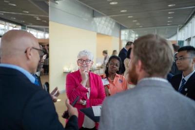 A group of people in business attire stand in a circle having a discussion in a modern indoor setting.
