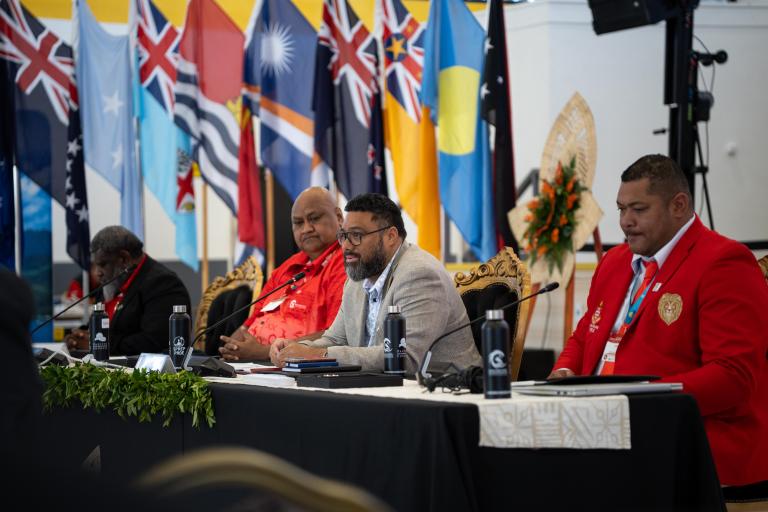 Hon. Lord Fatafehi Fakafanua Four men sit at a conference table with microphones and documents; various national flags are displayed in the background.