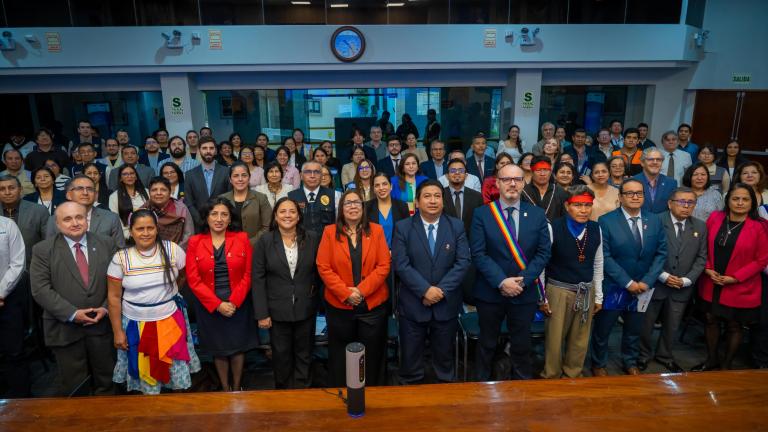 Photo 2__Closure Event in Peru.jpeg A large group of people, including men and women in formal and traditional attire, stand together in a conference room, facing the camera.