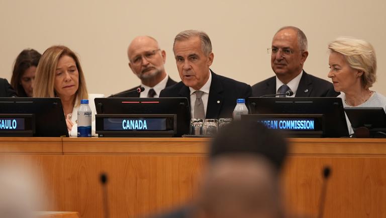 Mark Carney speaks at a table with nameplates for Canada and the European Commission, flanked by other representatives.