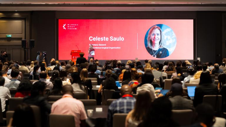 A speaker at the Global Heat Forum addresses an audience in front of a large screen displaying the name and photo of World Meteorological Organization Secretary-General Celeste Saulo.