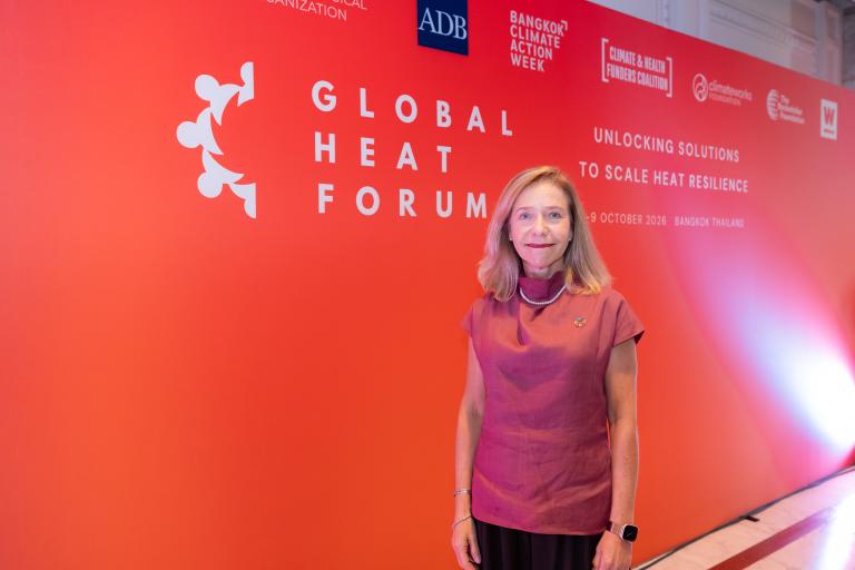 A woman stands in front of a red “Global Heat Forum” event backdrop featuring various organization logos.