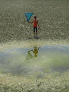 Child standing near a dry lake holding a kite