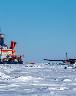 Two small planes on the ice next to a large ship.