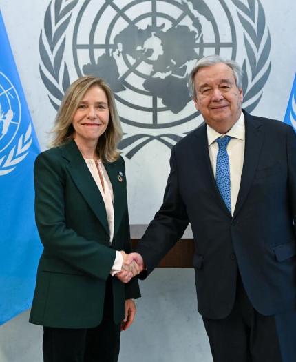 Two people shaking hands in front of un flags.