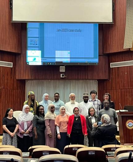 A group of people poses for a photo in front of a large screen displaying "Jan-2023 case study" in a wood-paneled auditorium.