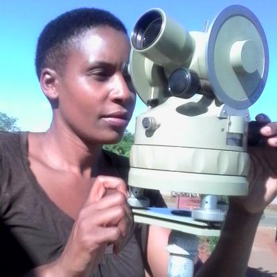 A person using a theodolite outdoors under a clear blue sky.