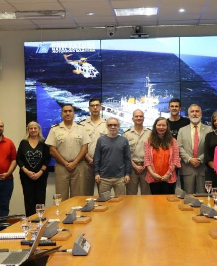 Group of people posing in a conference room with a large screen displaying a ship at sea in the background.