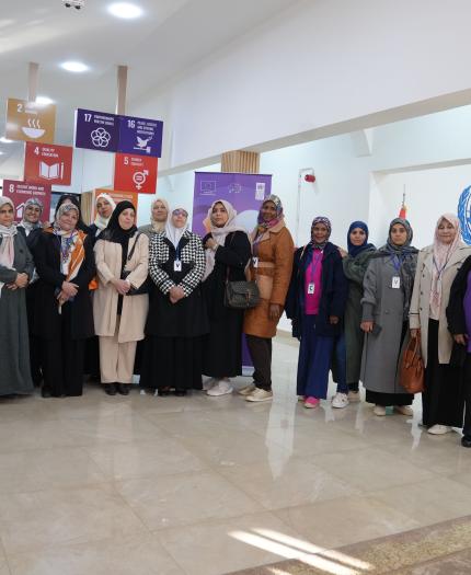 A group of people stands together indoors in front of colorful posters. Some are wearing badges and headscarves.