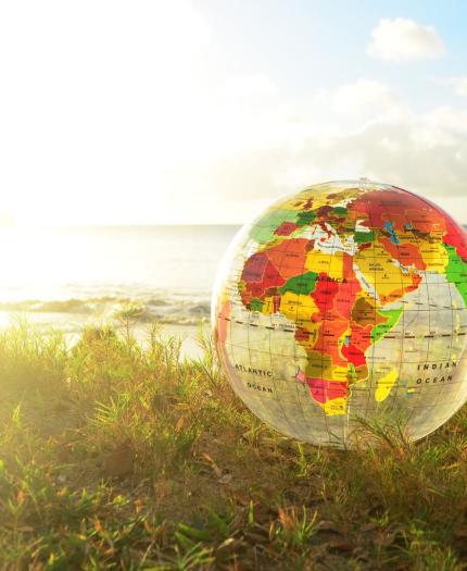 An inflatable globe sits on grass near a beach, with the ocean and sky in the background.