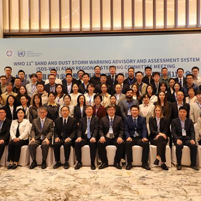 A large group of people in business attire pose for a group photo at the WMO 11th Sand and Dust Storm Warning Advisory and Assessment System meeting.