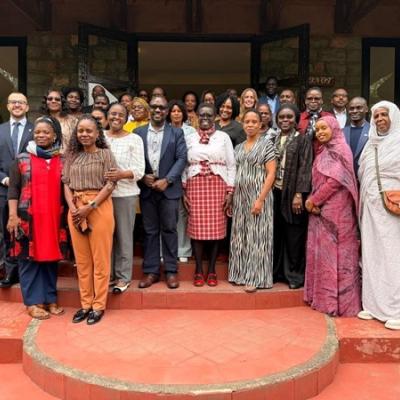 A large, diverse group of people stands together on red steps in front of a building, posing for a group photo.