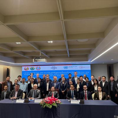 A group of people in business attire pose for a photo at a conference table, with a banner and flower arrangement in the background.