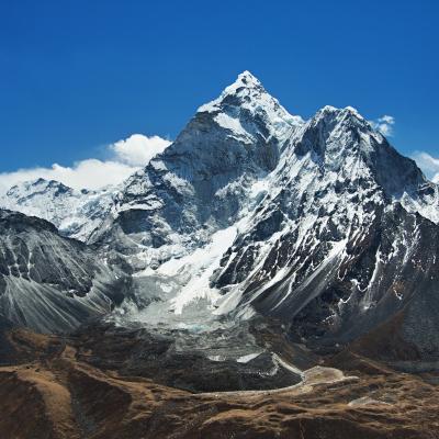 Snow-capped mountain peaks rise under a clear blue sky, with rocky slopes and patches of brown terrain in the foreground.