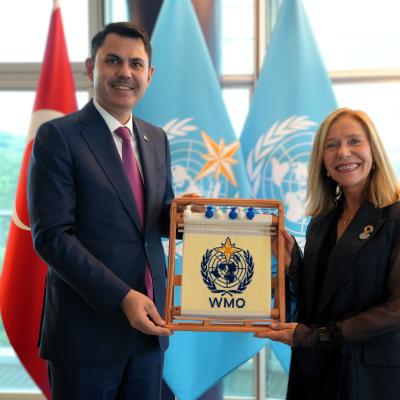 Two people stand indoors holding a framed WMO emblem, with the Turkish and WMO flags visible in the background.