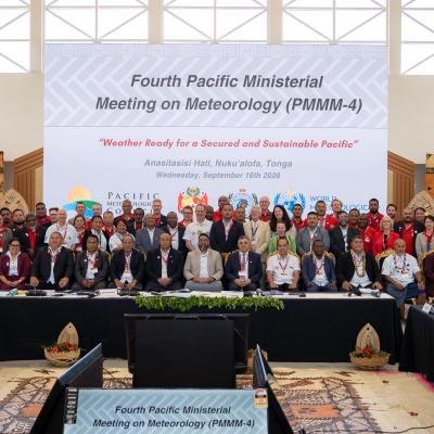 A large group of people poses for a photo at the Fourth Pacific Ministerial Meeting on Meteorology, with national flags and a conference banner in the background.