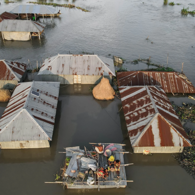 Aerial view of houses partially submerged in floodwater, with people on a makeshift raft in the center.