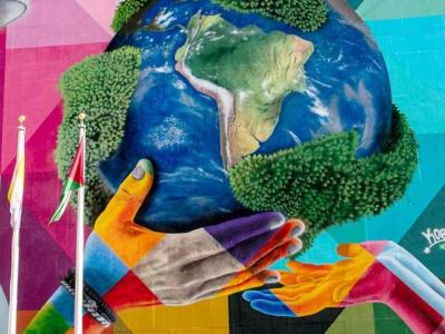 Colorful mural depicting a man and a child holding up a globe together, surrounded by vibrant geometric patterns.