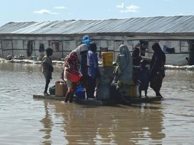 Families wade through floodwaters to access a water point