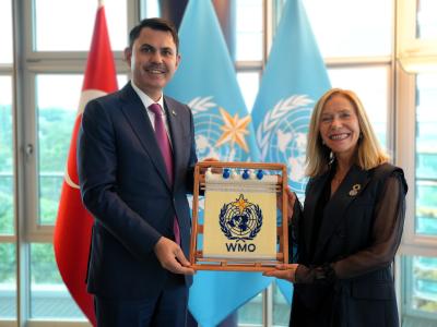 Two people stand indoors holding a framed WMO emblem, with the Turkish and WMO flags visible in the background.